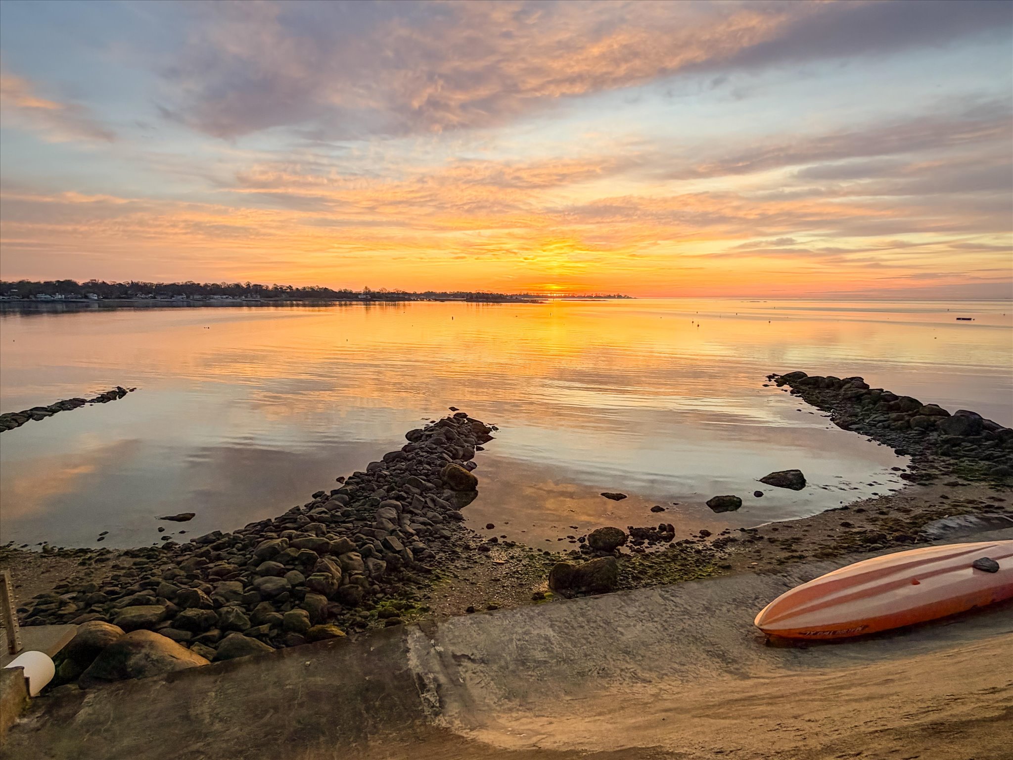 Sweeping coastal Connecticut shoreline at golden hour, calm blue water, dramatic amber sky